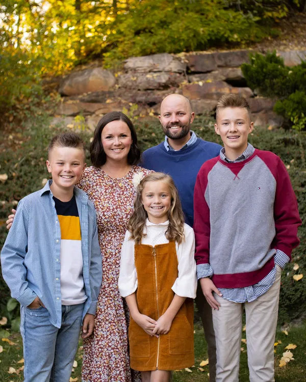 Family of five smiling together outdoors in autumn foliage