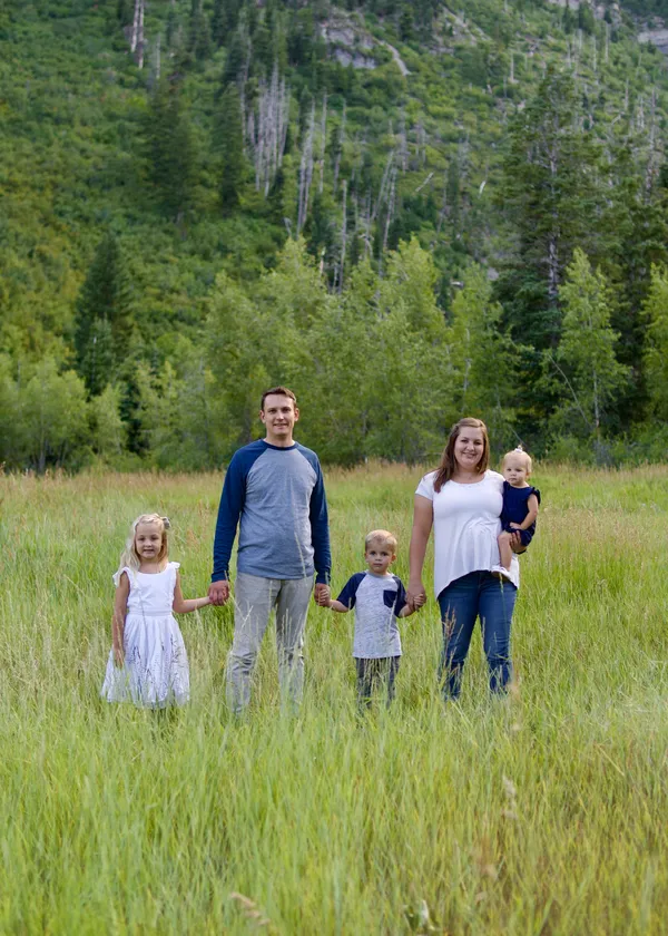 Family of five holding hands in a lush green mountain meadow