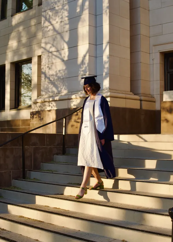 Woman in graduation cap and gown walking gracefully down steps in warm sunlight