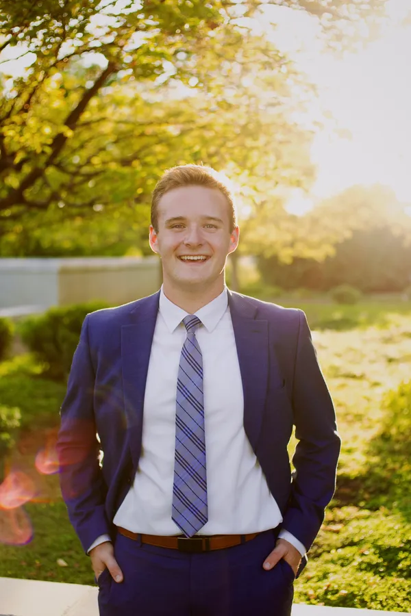 Young man in a navy suit smiling in golden afternoon light