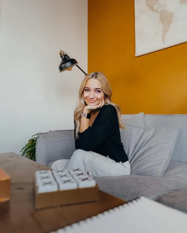 Young woman sitting relaxed on a couch smiling warmly in a cozy indoor setting