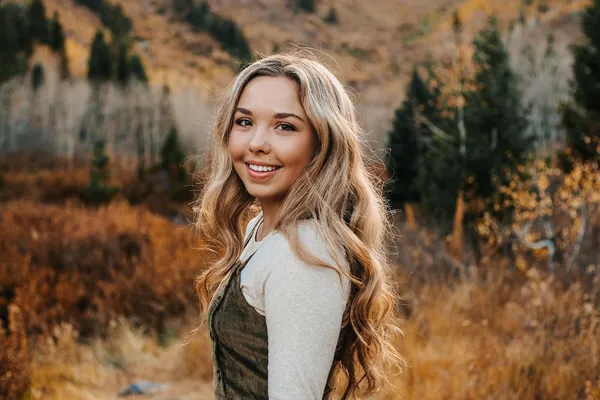 Young woman with long wavy hair smiling in an autumn mountain field with golden foliage