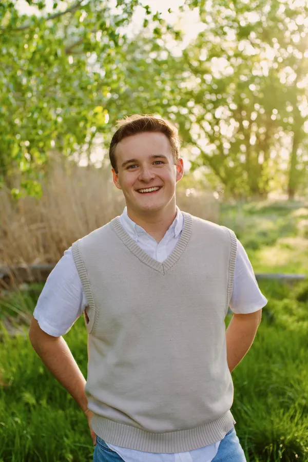 Young man smiling in soft golden hour light with green trees behind him