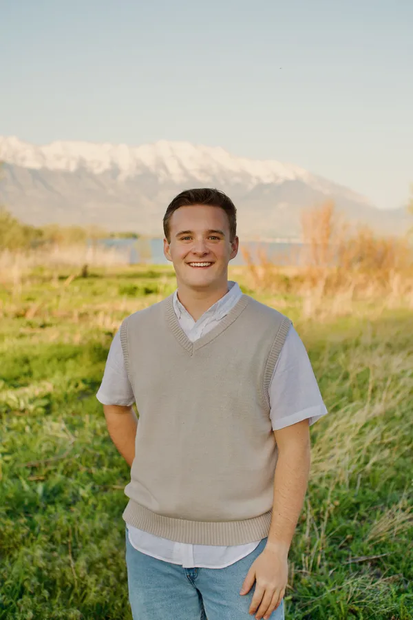 Young man standing in a green field with snow-capped mountains in the background