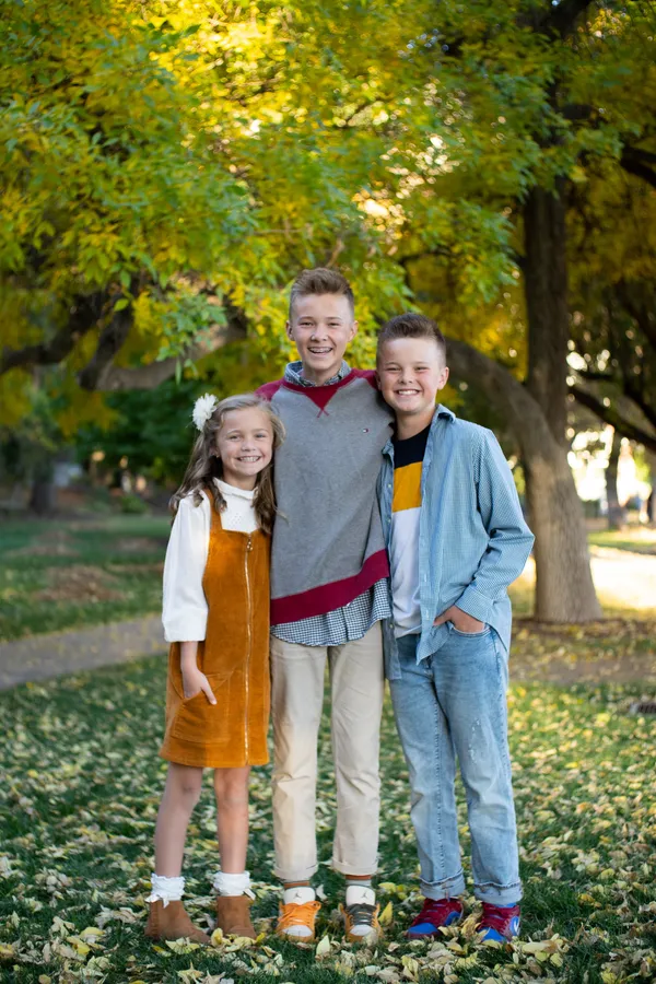 Three siblings laughing together under golden autumn trees